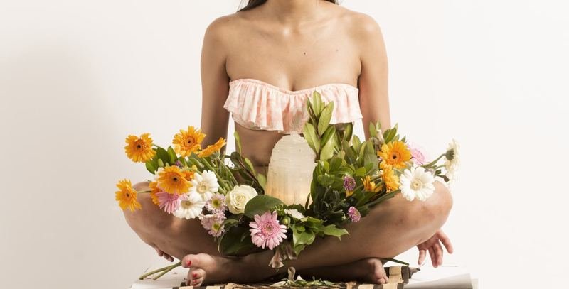 Une femme assise en tailleur tient contre son ventre une couronne de fleurs et une pierre de sélénite.