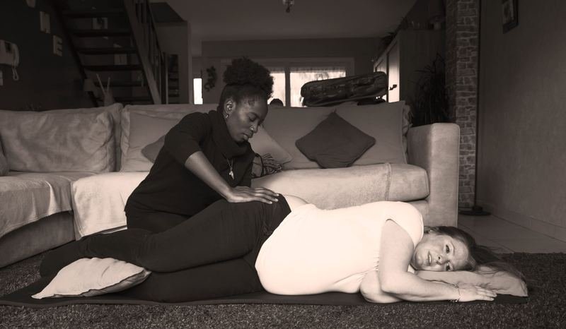 Gracia pose les mains sur le bas du dos d’une femme allongée sur le côté, au sol, dans un salon.